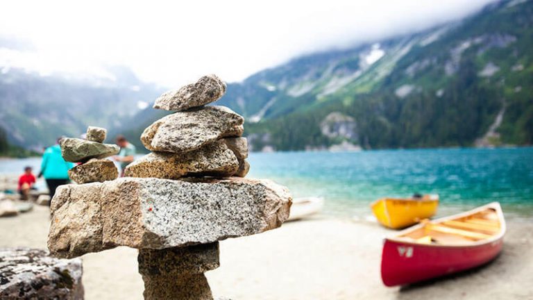 A rock sculpture and a canoe on the shore of a lake with a mountain in the background.