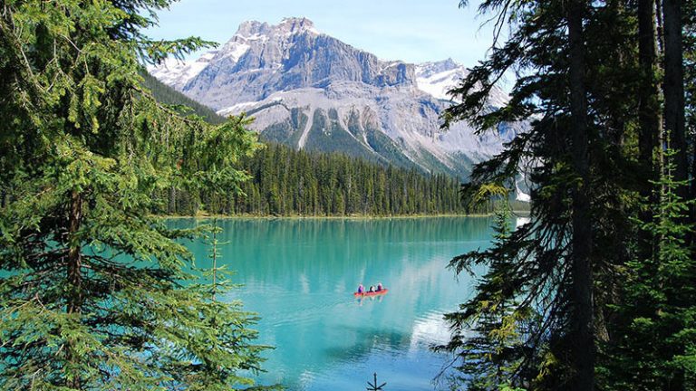 Les gens pagayent en canoë dans un lac, avec des arbres et une montagne en arrière-plan.